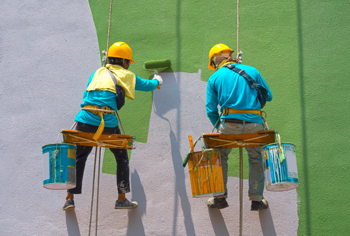 Two painters on suspended bosun's chairs rolling an exterior building wall