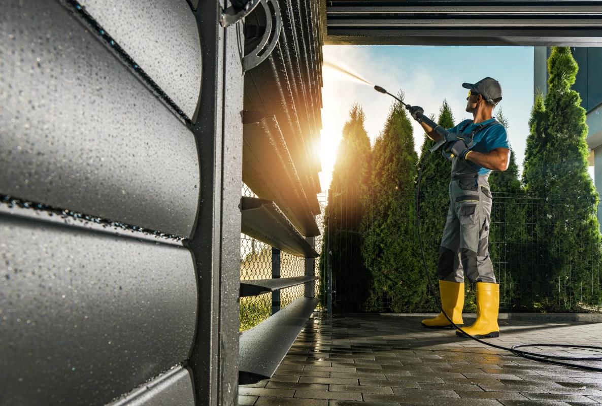 A worker pressure washing a building facade, clean surface against grimy