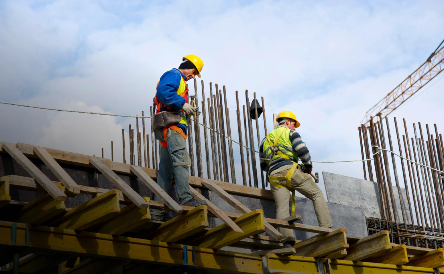 Two construction workers in high-visibility gear on scaffolding